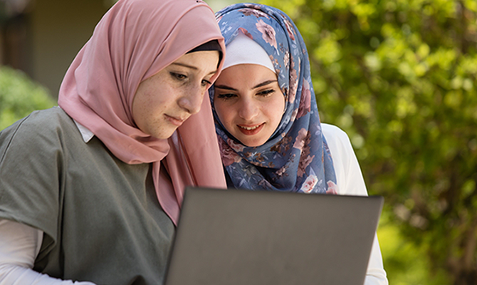 A photograph of two Muslim students working on a laptop.
